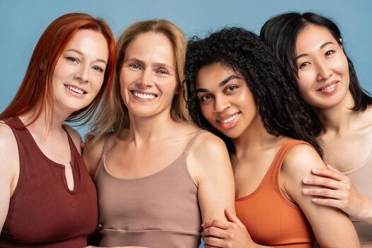 Four diverse, multinational women embracing, looking at camera, closeup posing in studio photo