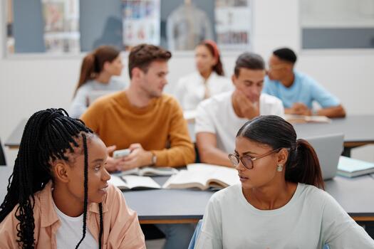 Students, classroom and college for learning, education and development. Women, university and friends together in conversation, study and discussion during lecture while at table in room on campus photo