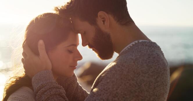 Couple, forehead touch and hug on beach together for romantic sunset, bonding in nature and love. Happy, man and woman embrace on ocean side for holiday, adventure and summer travel or vacation photo